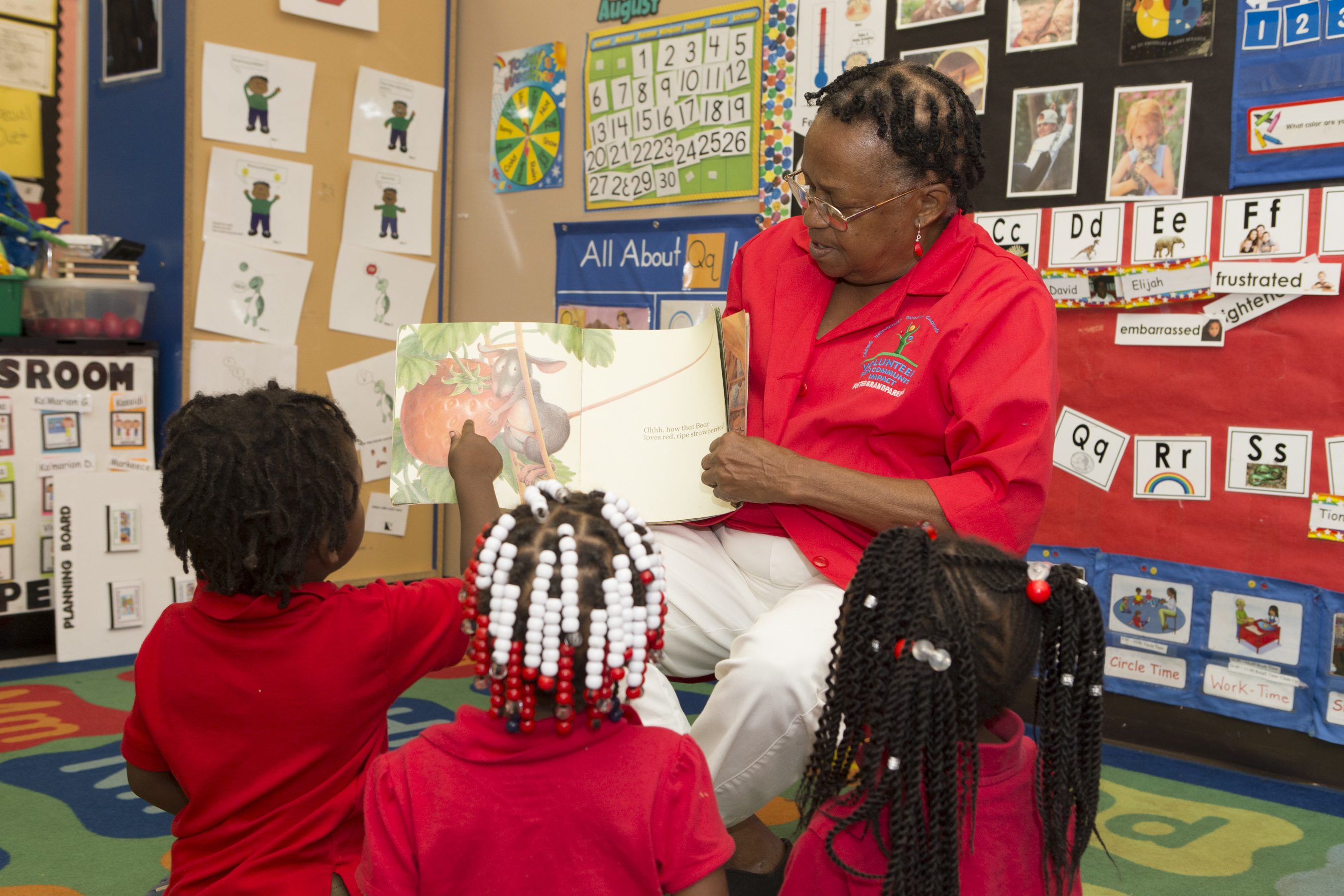 Una mujer les está leyendo un libro con ilustraciones a niños pequeños sentados en el suelo de un aula.